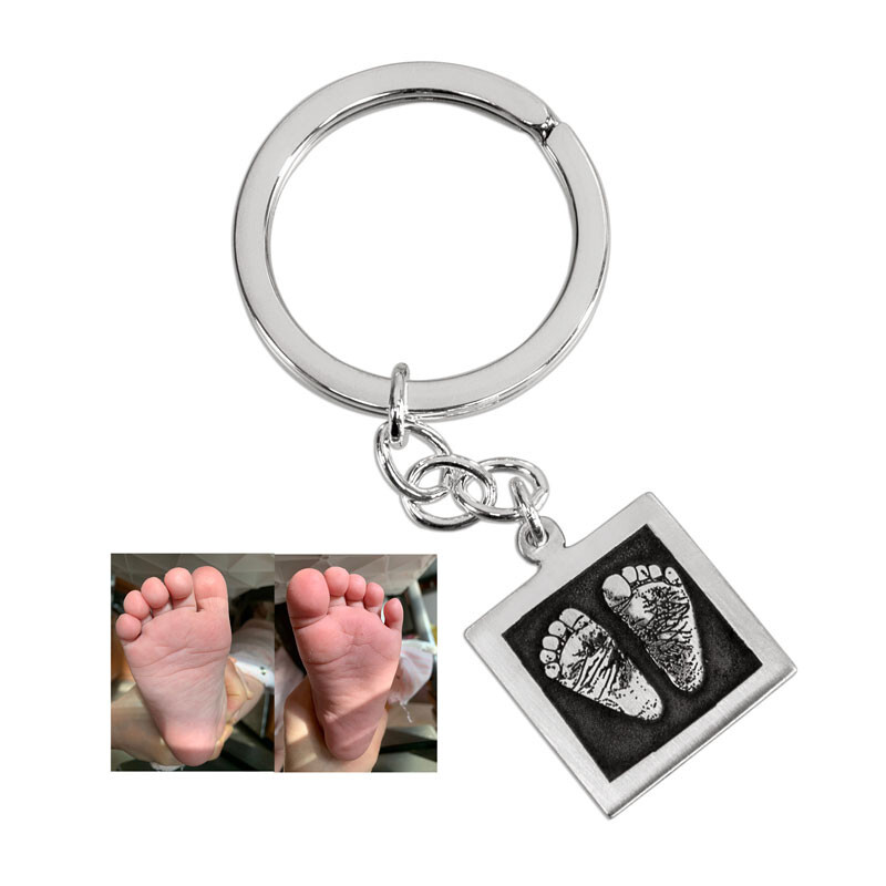 Silver keychain with baby's actual footprints engraved in bas relief, with a photo of the original footprints