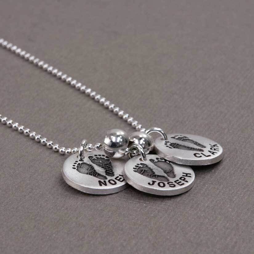 Silver necklace with 3 charms, shown from the side, with the actual footprints of the 3 kids engraved on it, along with their names - Heart On Your Wrist