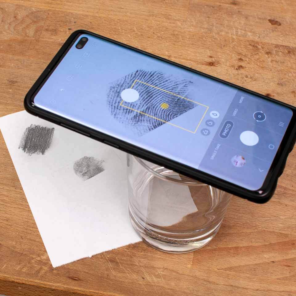 Phone in camera mode resting horizontally on a water glass to steady it for a photo of the paper below